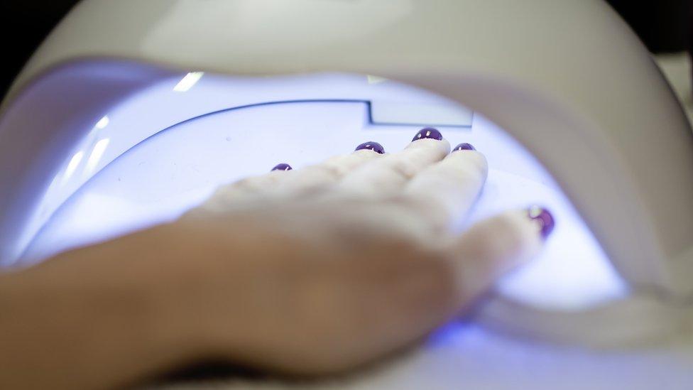 A woman places her hand under a UV lamp to dry her nails