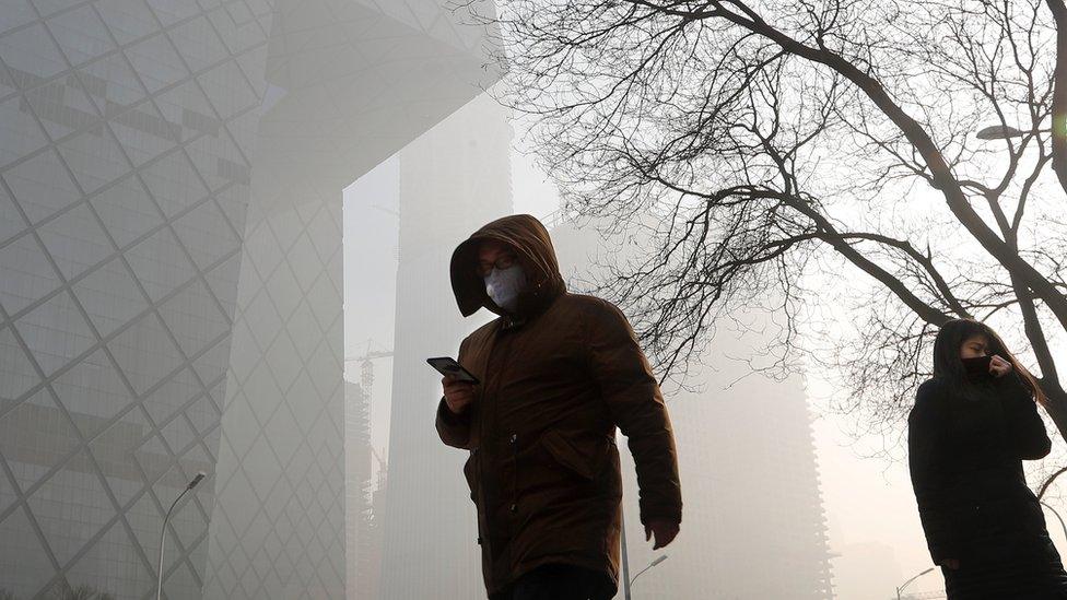 People wearing protection masks walk near the iconic headquarters of China"s state broadcaster Central China Television (CCTV) at the Central Business District in Beijing as the capital of China is blanked by heavy smog on 3 January