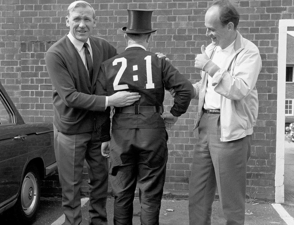 A West Germany fan dressed as a chimney sweep (a German symbol of good luck) is congratulated on his prediction for the World Cup Final scoreline by team advisor Bert Trautmann (left) and press officer Wilfried Gerhardt (right) as they meet outside the team's hotel on 30 July 1966, the morning of the final