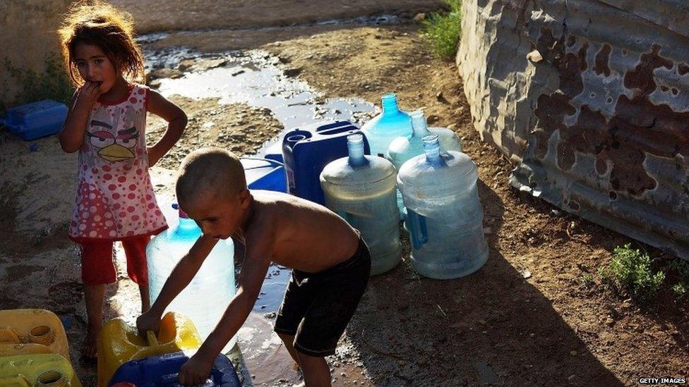 Syrian children fill jerry cans with water at a pump inside a camp for refugees in Baalbek, Lebanon