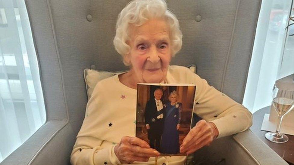 Rosina Clifton holding up her telegram from King Charles, which features a photo of King Charles and the Queen consort.