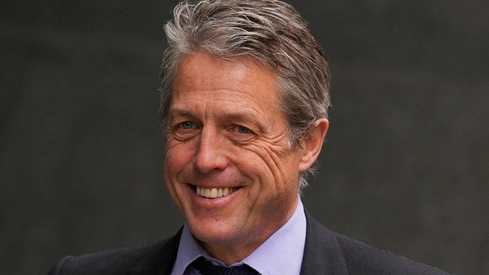 Hugh Grant smiles outside the High Court, in London