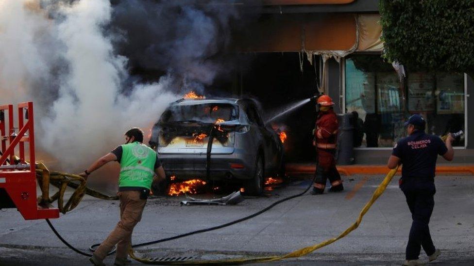 Firefighters work on a burning car outside a store after an operation by security forces against organized crime in Celaya, in Guanajuato state, Mexico June 20, 2020