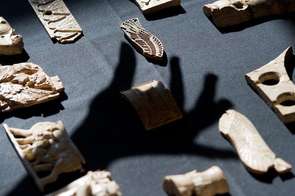 Shadow of hand over Assyrian objects on a table