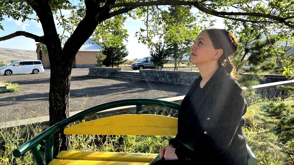 Vera Khachatryan sits on a bench by St Gayane Church in Jermuk, Armenia