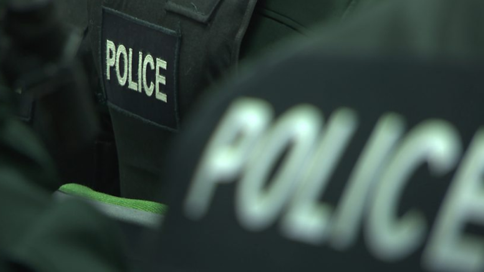 Close up of the back of two police officers wearing black jackets with police written on them