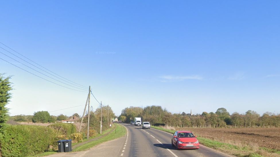 A streetview of the A10, with a blue sky above. The low sun is casting a shadow over the passing cars which are travelling towards the camera.