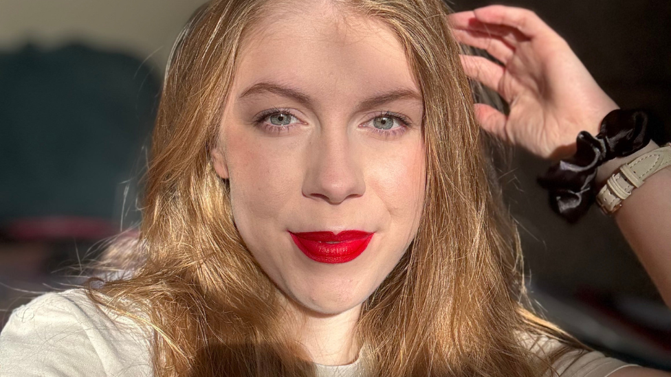 Fay Crockett is looking towards the camera with a slight smile. She has long blond hair and is wearing red lipstick