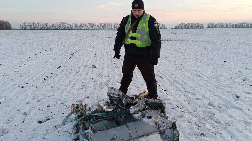 A Ukrainian policeman stands over a fragment of a Russian missile