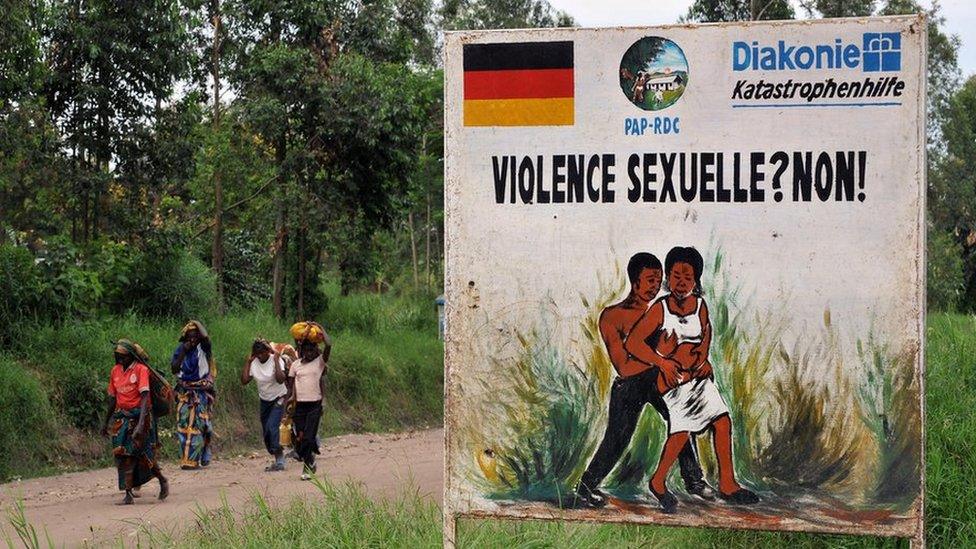 Congolese women walk past a sign opposing sexual violence on December 4, 2008 in Nyamilima, in Nord-Kivu, in the east of the Democratic Republic of Congo (DRC).