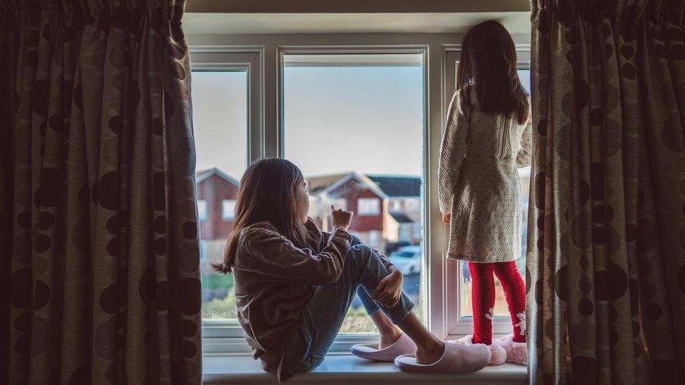 Two girls staring sitting on a window ledge staring out on the street