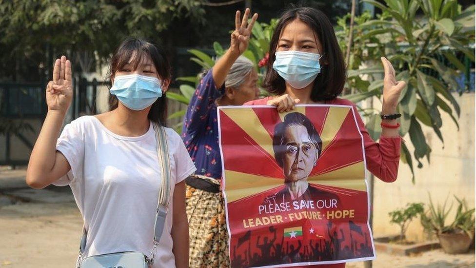 Demonstrators flash the three-finger salute while holding an image of detained leader Aung San Suu Kyi