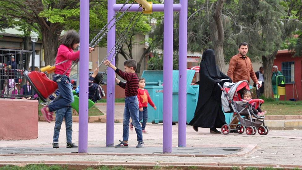 Children playing in a predominantly Syrian neighbourhood in Gaziantep, where a family walk past with the mother wearing a black veil