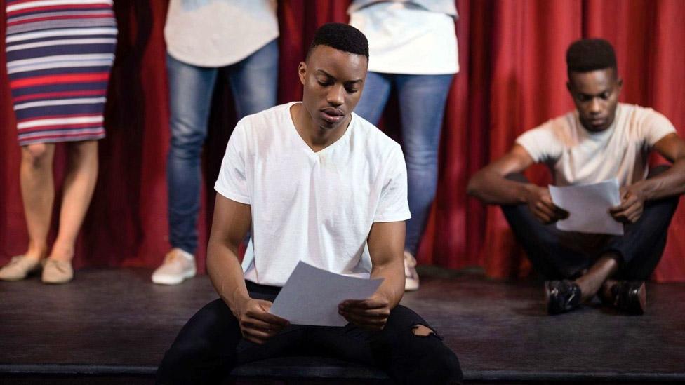 Staged photo depicting actors reading scripts