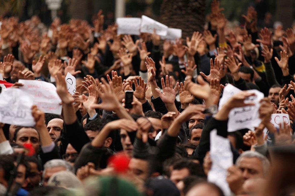 Tunisian demonstrators gesture with their hands calling to the army to pull down the Constitutional Democratic Rally (RCD) party headquarters sign on January 20, 2011 in Tunis, Tunisia.