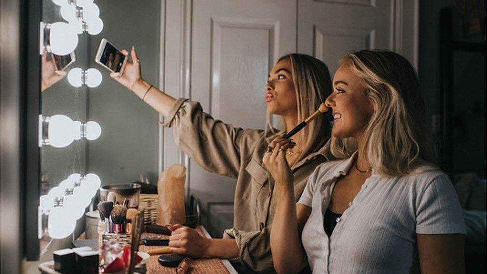 Two women doing make-up with phone