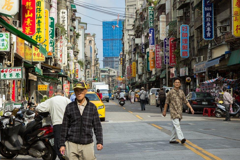 People and vehicles at a street and buildings full of signboards in Taipei, Taiwan.