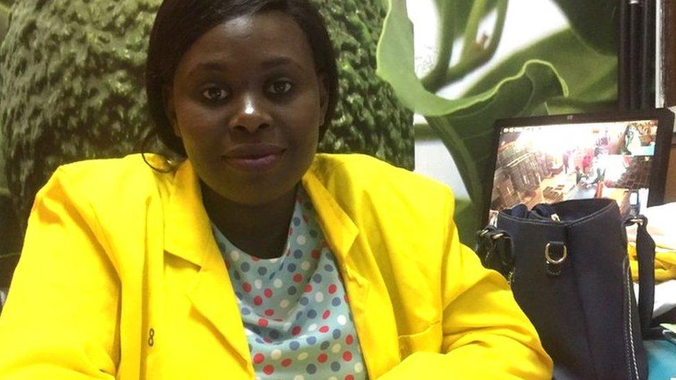 Lucy Njeri, the co-owner of Saipei foods, sits at her desk with a laptop and a TV monitor showing work in the packing house