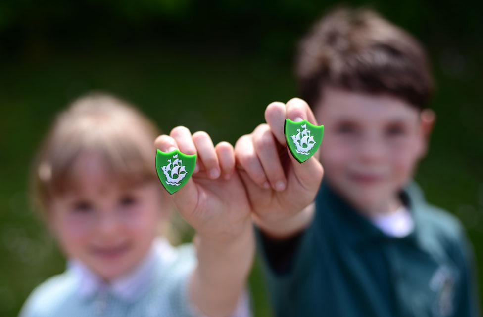 A girl and a boy hold up a green Blue Peter badge