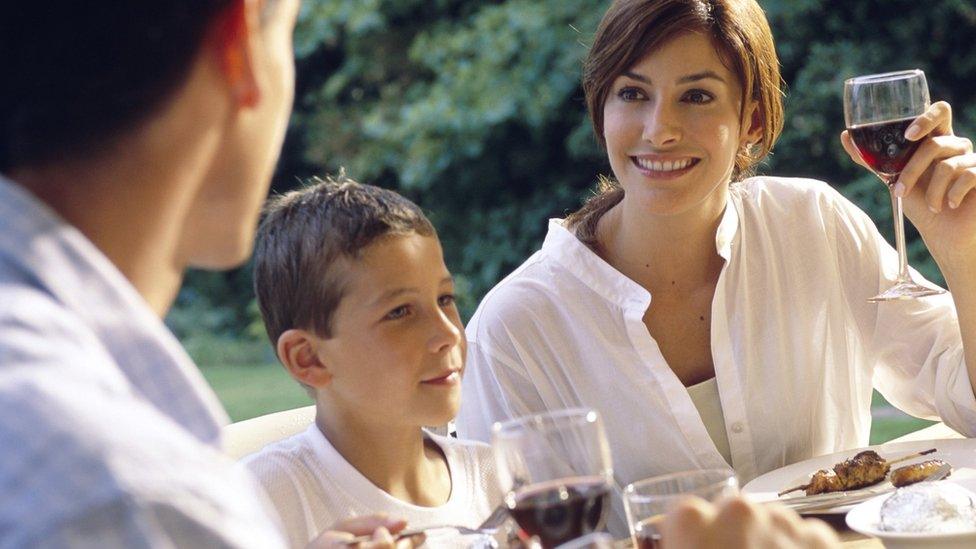 A couple drinking wine, sat with a young boy