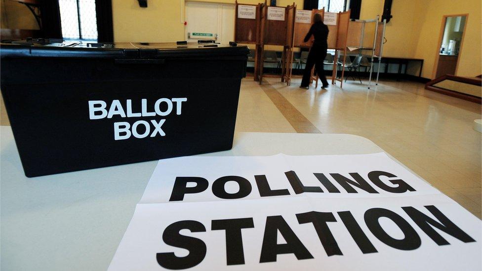 A ballot box shown with polling booths in the distance