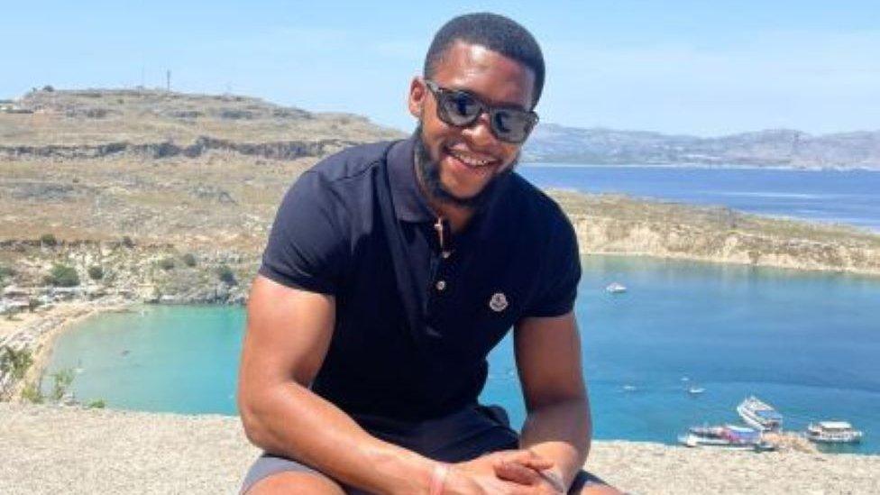 Theo Porteous pictured sitting on a stone wall with the ocean behind him.