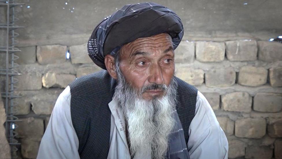 Noor Mohammed sits in front of a wall in brick building