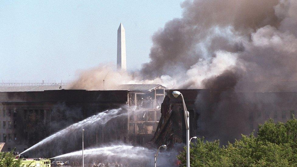 The Washington Momument stands in the background as firefighters pour water on a fire at the Pentagon that was caused by a hijacked plane crashing into the building September 11, 2001 in Washington, DC