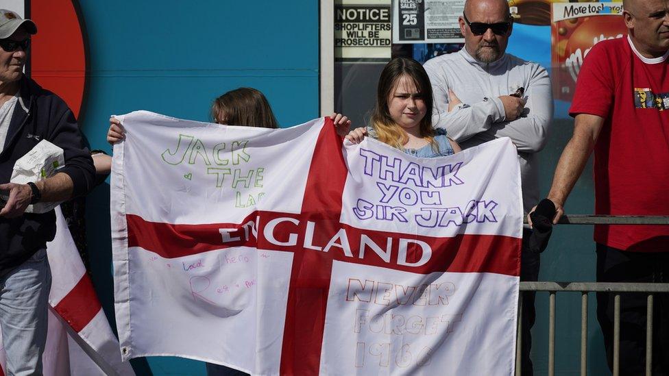 Two youngsters hold up an England flag with messages celebrating Jack Charlton