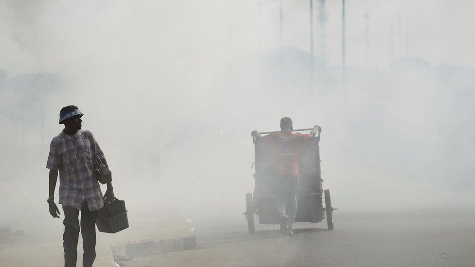 A local cobbler walk past smoke emitting from a dump