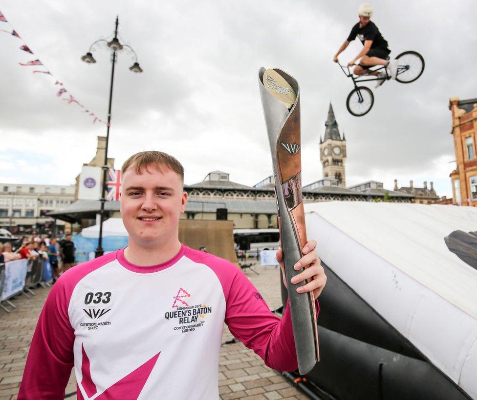 Cameron Stewart holds the baton in Darlington as a BMX rider performs a stunt in the background