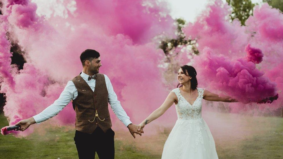 Marries couple pose for wedding photo with pink smoke bombs in the background