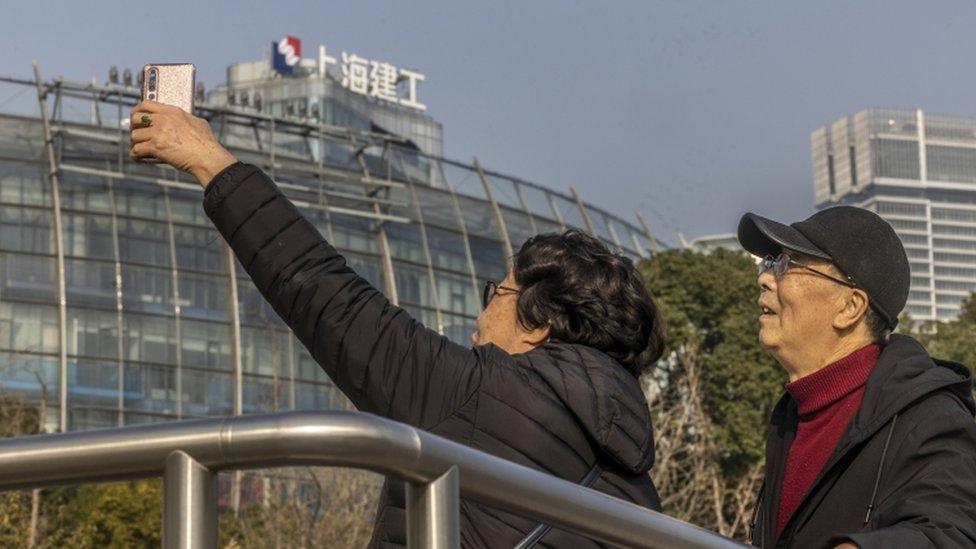 People stand in front of the Evergrande Centre from which logo has been removed.