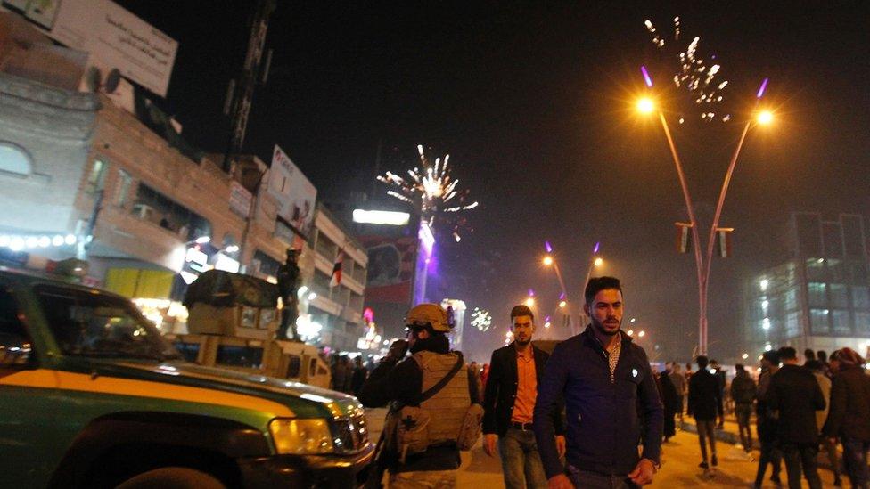Iraqi walk past security forces as they gather at the al-Mansour square during Christmas and New Years eve celebrations in the capital Baghdad