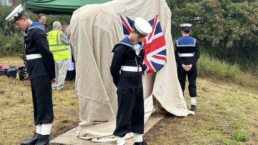 Three young people in sea cadet uniform stand around the horse sculpture