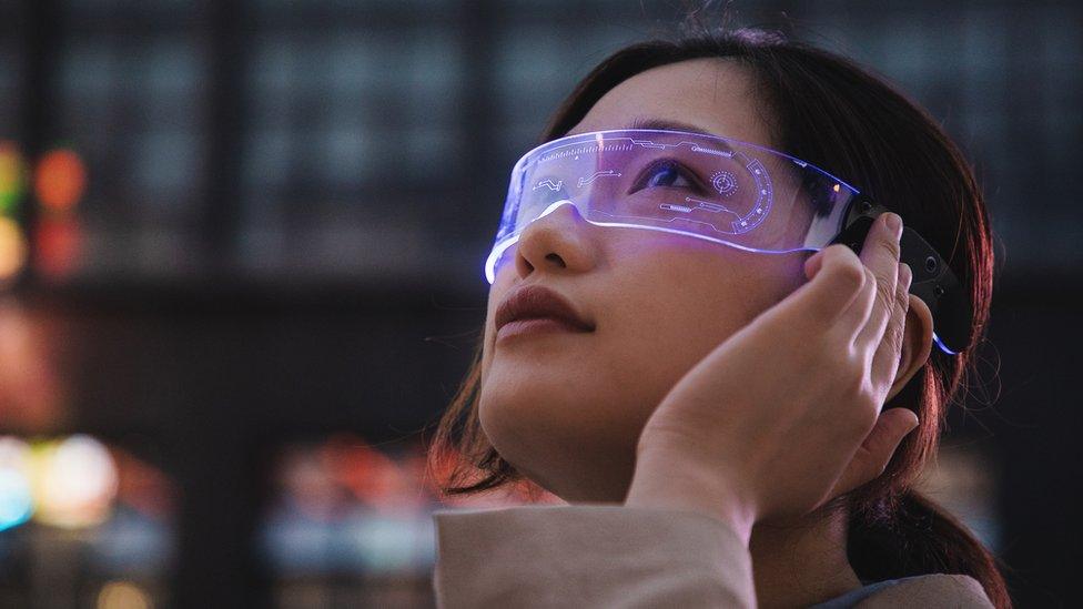 A young woman wears a glass visor with futuristic-looking text and graphics floating across her vision