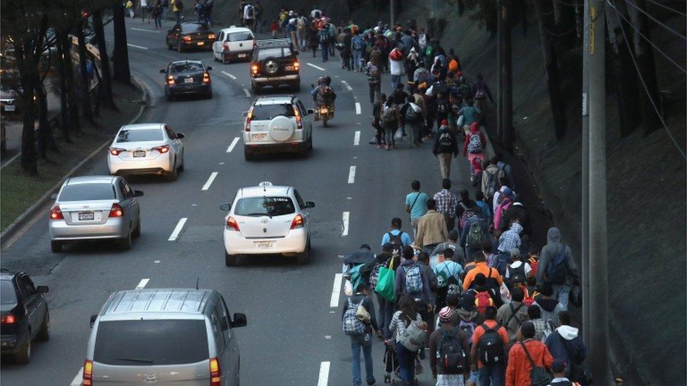 Migrants walk alongside cars on a road