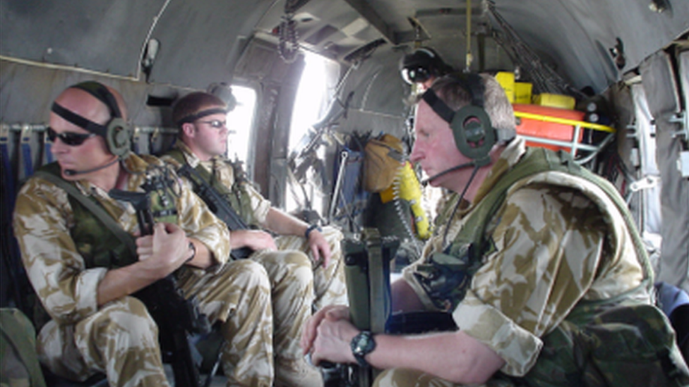 Brigadier Moore watching the Basra riots from helicopter in 2003 wearing a headset and holding rifle