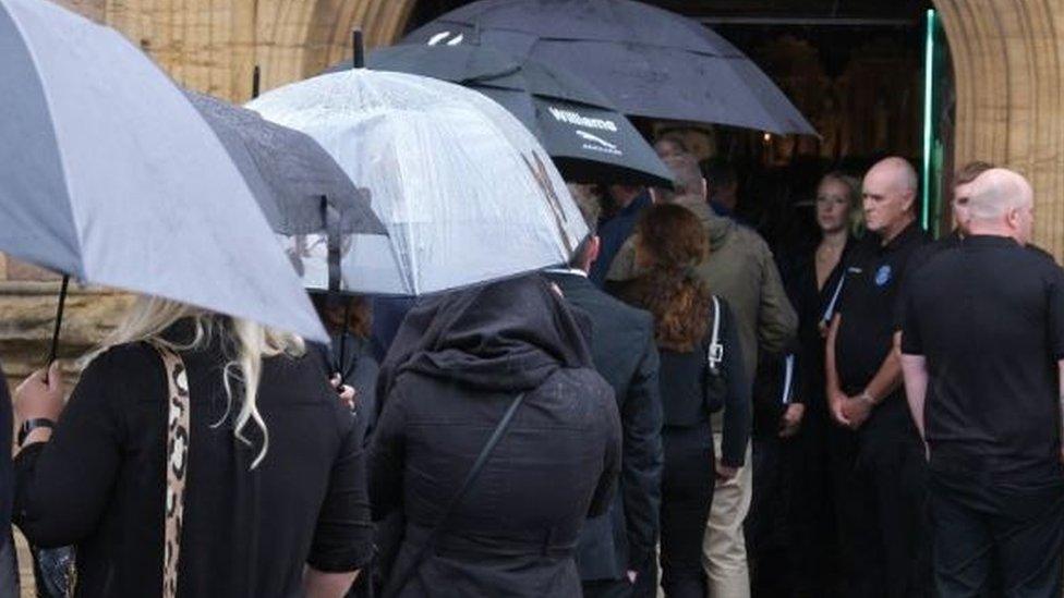 Mourners holding umbrellas while filing into a church