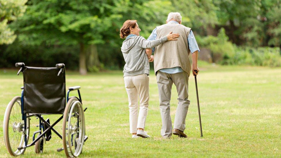 Woman helps man walk with a stick