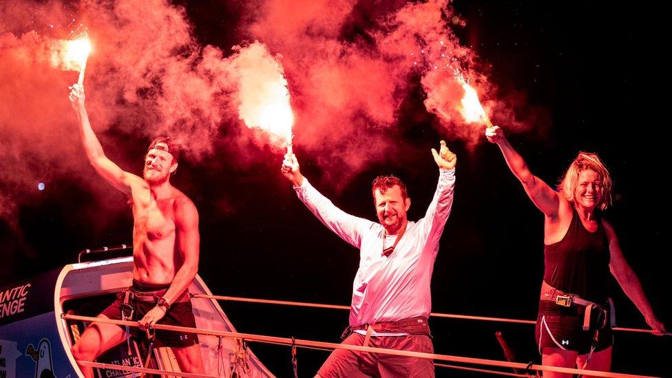 Rowers from team Ready to Row holding flares at the finish line in Antigua