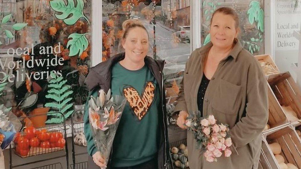 Two women standing outside a florist holding bunches of flowers