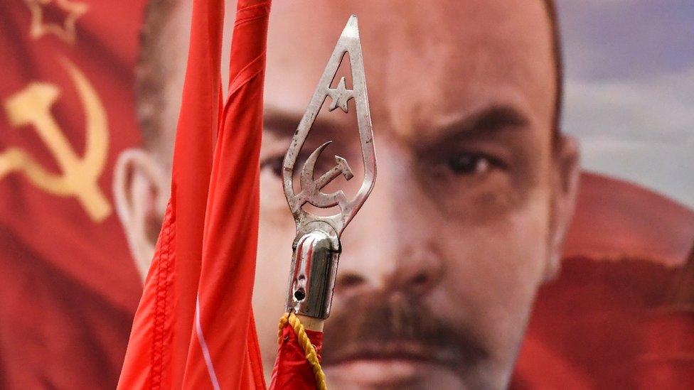 A picture of Vladimir Lenin behind a standard showing the communist symbol