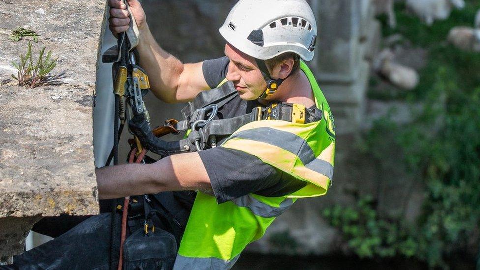 A stonemason suspended on climbing ropes at the Dundas Aqueduct