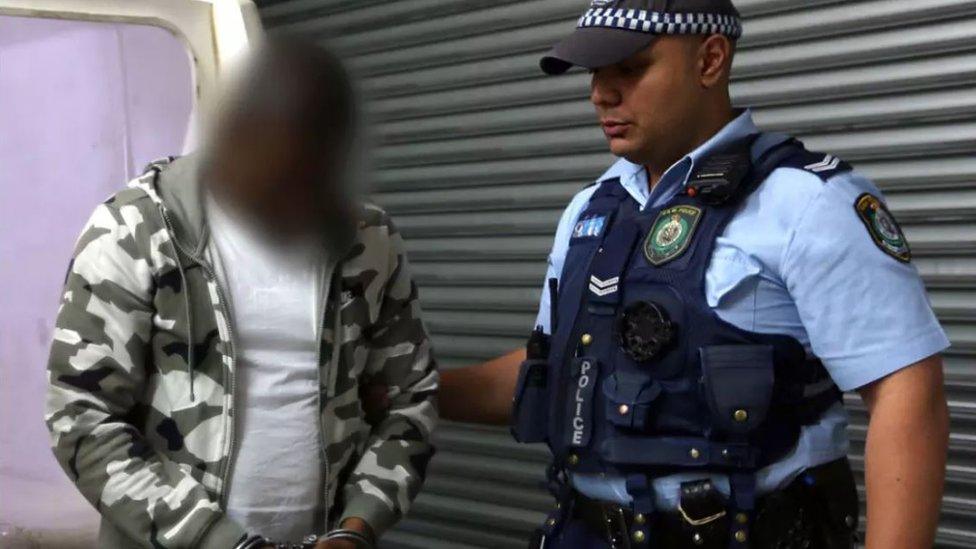 The alleged ringleader, shown in an image blurred by New South Wales Police, is accompanied by a police officer