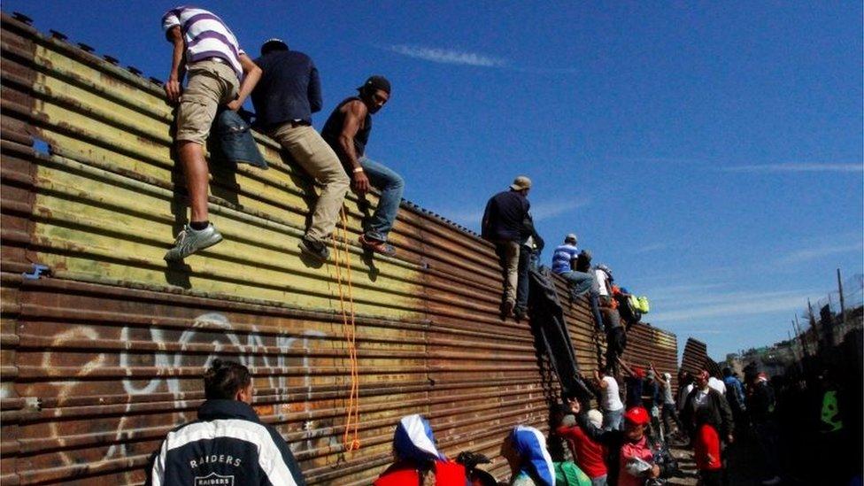 Migrants climb the border fence between Mexico and the United States