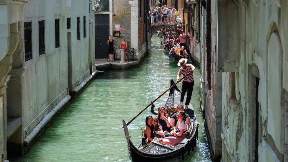 Gondoliers row their gondolas through the Venice Canal