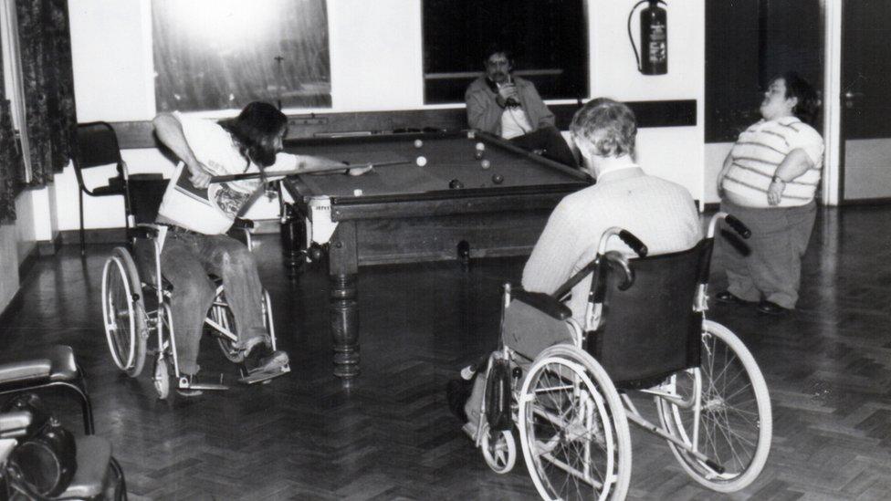 Four men, three wheelchair users and a man with dwarfism playing pool