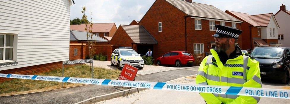 A police officer guards the entrance to a housing estate in Muggleton Road