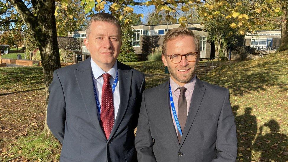 Two men in suits by trees in a school grounds